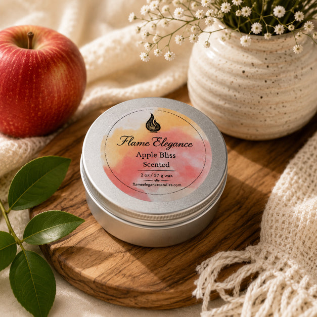 A round silver tin of Flame Elegance Apple Bliss Scented wax sits on a wooden board, styled with a red apple, green leaves, cream knit fabric, and a ceramic vase with small white flowers.