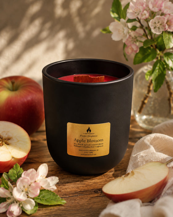 Black glass vessel labeled 'Apple Blossom' with apples and flowers on a wooden surface. Candle is red with wood wick by Flame Elegance