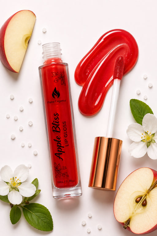 Apple Bliss Lip Gloss by Flame Elegance in a clear tube with a rose gold cap, shown with the applicator and a glossy red smear on a white background, styled with apple slices, white flowers, and green leaves.