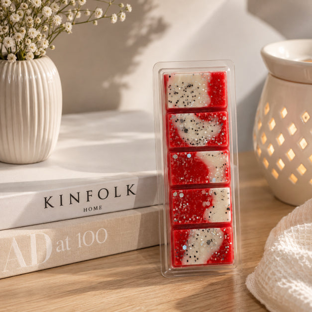 Pack of red and white wax melts scented with Apple Bliss soy wax on a wooden surface with books and a vase in the background.