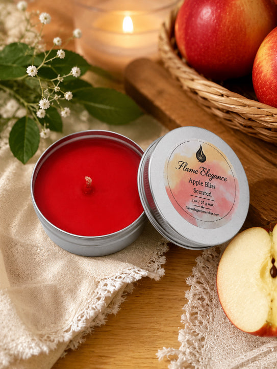 An open round metal candle tin filled with bright red wax sits beside its matching lid on a wooden surface. The lid label reads 'Flame Elegance Apple Bliss Scented.