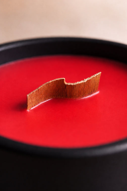 Red candle scented with apple bliss fragrance with a curved wood wick in a black container by Flame Elegance