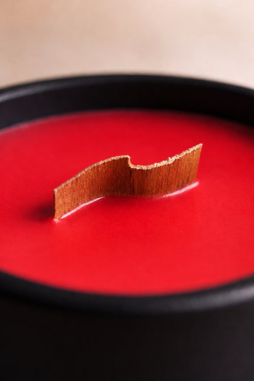 Red candle scented with apple bliss fragrance with a curved wood wick in a black container by Flame Elegance