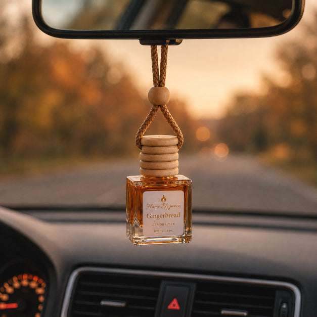 A car air freshener bottle labeled Flame Elegance Gingerbread' hanging from a rearview mirror with a rope loop in a car interior at sunset.