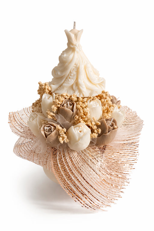 sculpted candle shaped like a wedding dress on top of taupe and cream tulip candles scented with love spell fragrance adorned with baby's breath and in a white keepsake box by flame elegance. White background. 