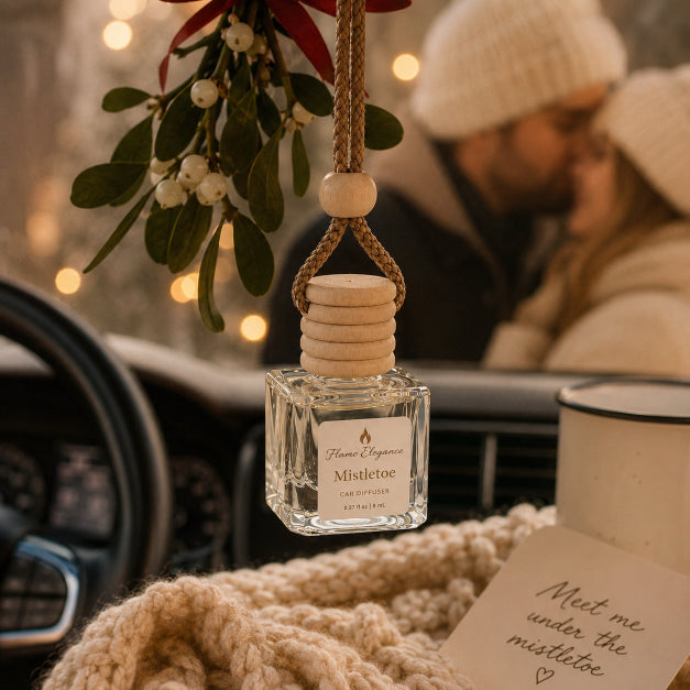 A festive mistletoe-themed car diffuser bottle hanging in a car interior, with a blurred couple in the background, a knit blanket, and a handwritten note in the foreground by Flame Elegance