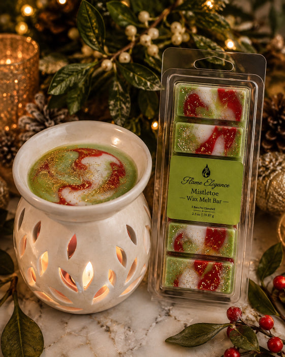 A package of five mistletoe scented wax melts by Flame Elegance next to a white ceramic wax warmer filled with a green and red swirled wax blend, styled on a marble surface with holiday greenery and warm lights in the background.