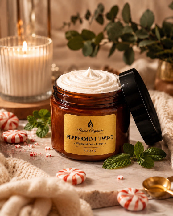 An amber glass jar candle with whipped body butter visible at the top, labeled 'Flame Elegance Peppermint Twist,' shown with its black lid leaning beside it. The scene is styled with peppermint candies, mint leaves, a lit candle, and soft neutral textiles in a warm, cozy setting.