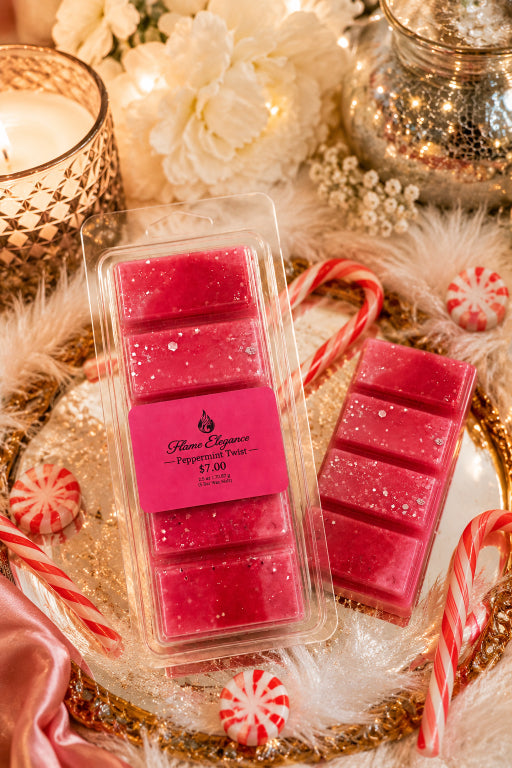A packaged set of bright pink wax melts with a matching pink label reading Flame Elegance Peppermint Twist $7.00,' styled on a gold tray with candy canes, peppermint candies, faux fur, and warm holiday decor.