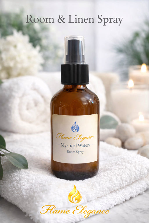 Room & Linen Spray bottle labeled 'Mystical Waters' by 'Flame Elegance' on a white towel with candles and flowers in the background.
