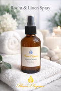 Room & Linen Spray bottle labeled 'Mystical Waters' by 'Flame Elegance' on a white towel with candles and flowers in the background.