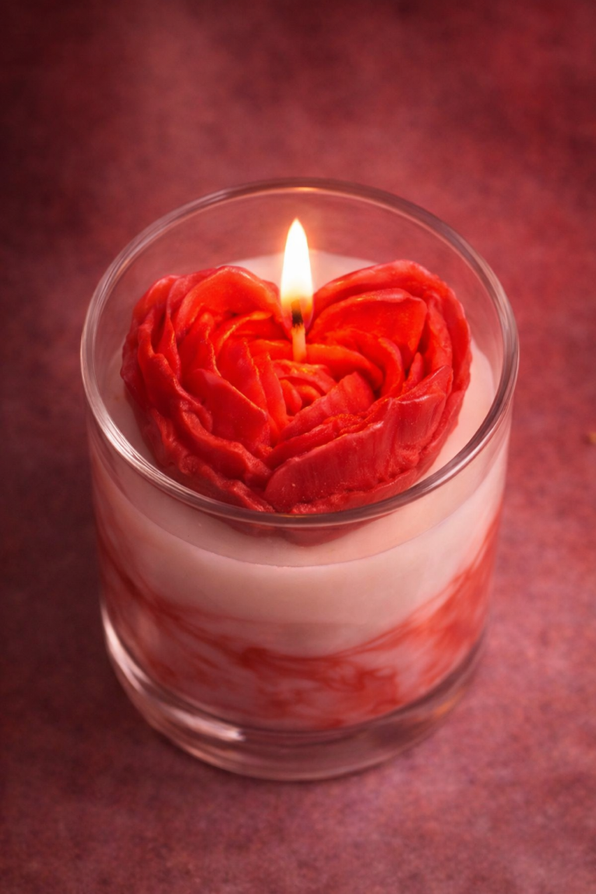 Candle in a glass holder with a heart-shaped red rose design on a red background