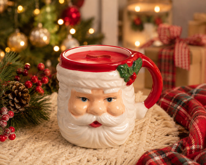 Santa mug with red candle scented with sugar plum and crackling wood wick with holiday background including christmas tree packages and red plaid blanket. Candle by Flame Elegance. 