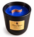 A black ceramic soy candle jar with a vibrant blue wax fill and a wavy wooden wick. The front features a gold label with the brand 'Flame Elegance' and scent name 'Sapphire Desire'.