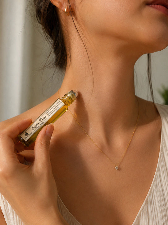 Person applying a small bottle of Sapphire Desire luxury body perfume  oil to their neck with a blurred background by Flame Elegance
