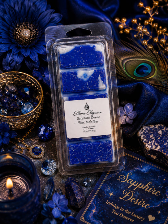 A packaged wax melt bar set labeled Flame Elegance Sapphire Desire, shown in a clear plastic clamshell with four blue wax sections and a white label. The product is styled on dark blue fabric with peacock feathers, crystals, a lit candle, and decorative props.