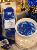 Flame Elegance Sapphire Denim wax melts shown in a clear plastic package next to a white ceramic scented candle holder filled with blue and white marbled wax and gold glitter.
