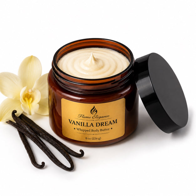 An open amber plastic jar of Flame Elegance Vanilla Dream Whipped Body Butter with its black lid leaning against it, shown on a white background with vanilla beans and a vanilla flower as props.