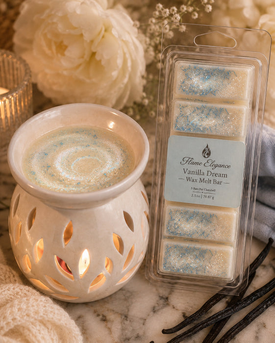 A packaged wax melt bar set labeled Flame Elegance Vanilla Dream sits beside a lit white ceramic wax warmer with a candle-like wax pool and warm light. The scene is styled with cream flowers, a candle, and vanilla beans on a soft neutral background.