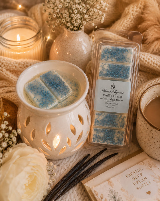 A packaged wax melt bar labeled Flame Elegance Vanilla Dream sits on a cozy styled surface with a lit white wax warmer, candles, flowers, and vanilla beans. The product is shown in a real, warm, home-like setting rather than isolated on a plain background, so this fits Lifestyle.