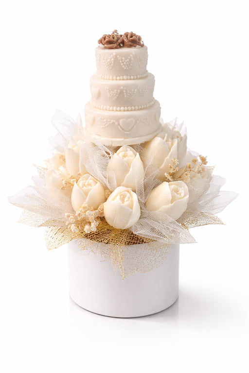 Three tiered ivory soy wax wedding cake candle sitting on top of a bed of candle tulips in a white keepsake box scented with champagne toast fragrance by Flame Elegance. White background. 