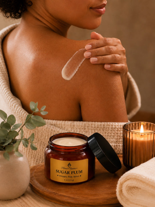 Person applying Sugar Plum whipped body butter by Flame Elegance  to their shoulder with a jar of 'Sugar Plum' body butter on a wooden tray.